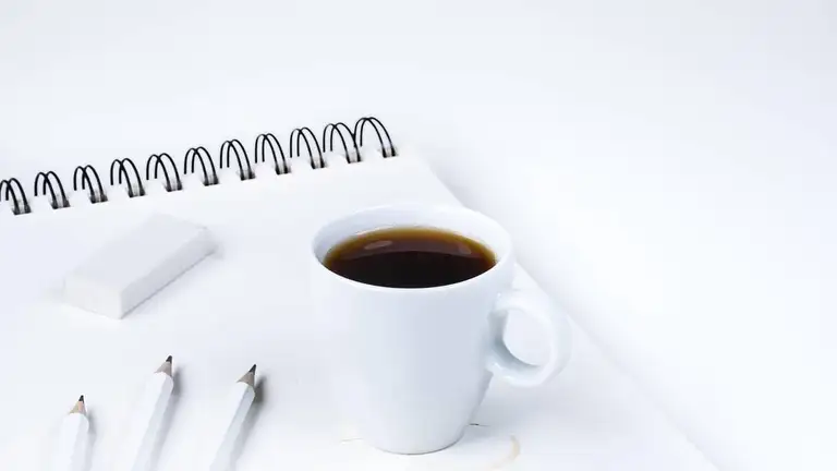 Radiergummi, Bleistifte und Kaffeetasse auf einem Notizblock