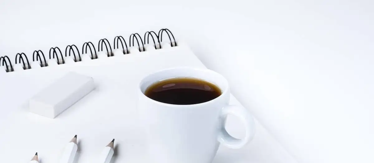 Radiergummi, Bleistifte und Kaffeetasse auf einem Notizblock
